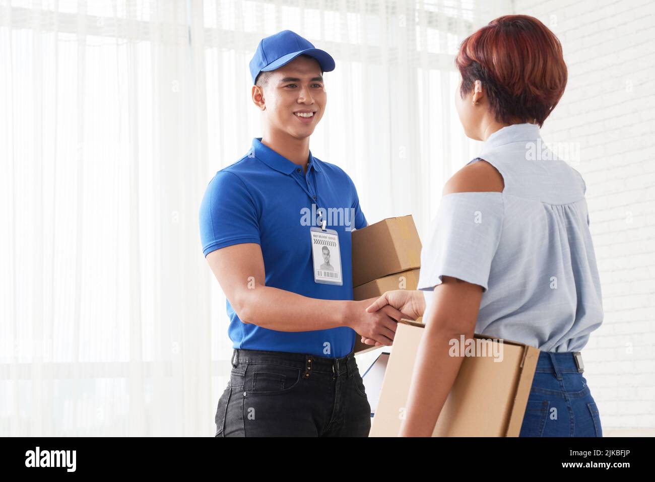 Fröhlicher asiatischer Lieferer schüttelt die Hand des Kunden Stockfoto