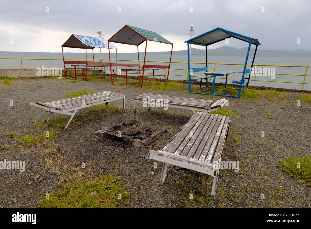 Alte Liegestühle und farbenfrohe Pavillons am Sevan-Ufer bei windigem Wetter Stockfoto