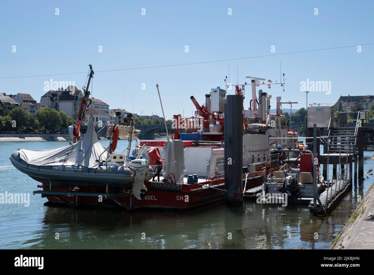 Rot-weißes Feuerlöschboot mit kleineren Gummilifebooten, die an einem sonnigen Sommertag am Rheinufer in der Stadt Basel festgemacht wurden Stockfoto