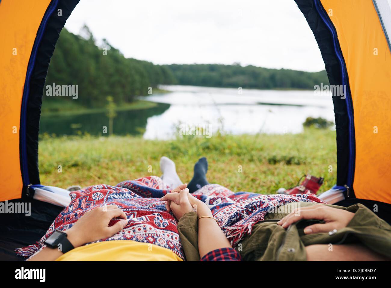 Zugeschnittenes Bild eines Paares, das die Hände hält, wenn es im Zelt am See liegt Stockfoto