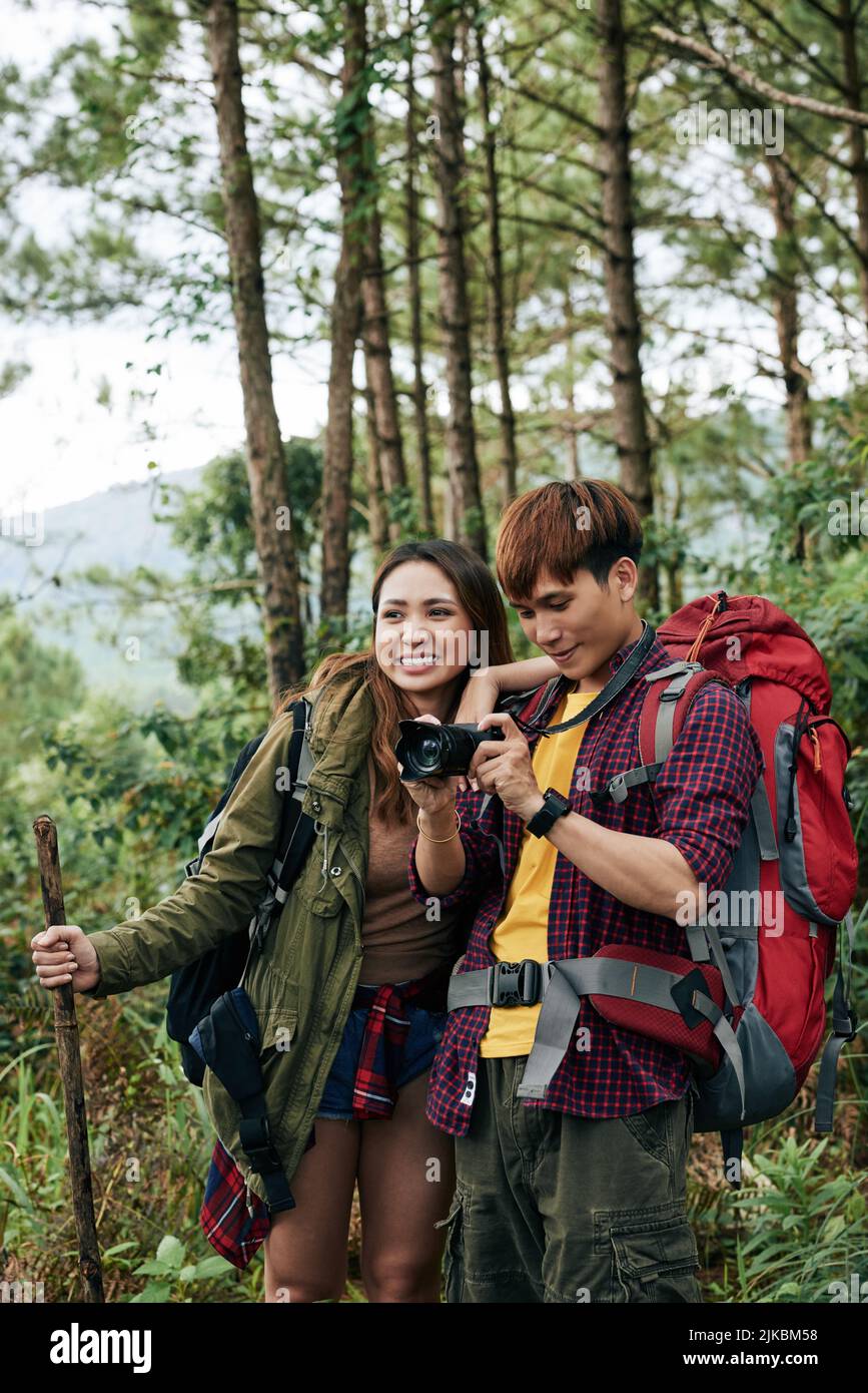 Fröhliches junges asiatisches Paar, das im Wald wandert und Fotos fotografiert Stockfoto