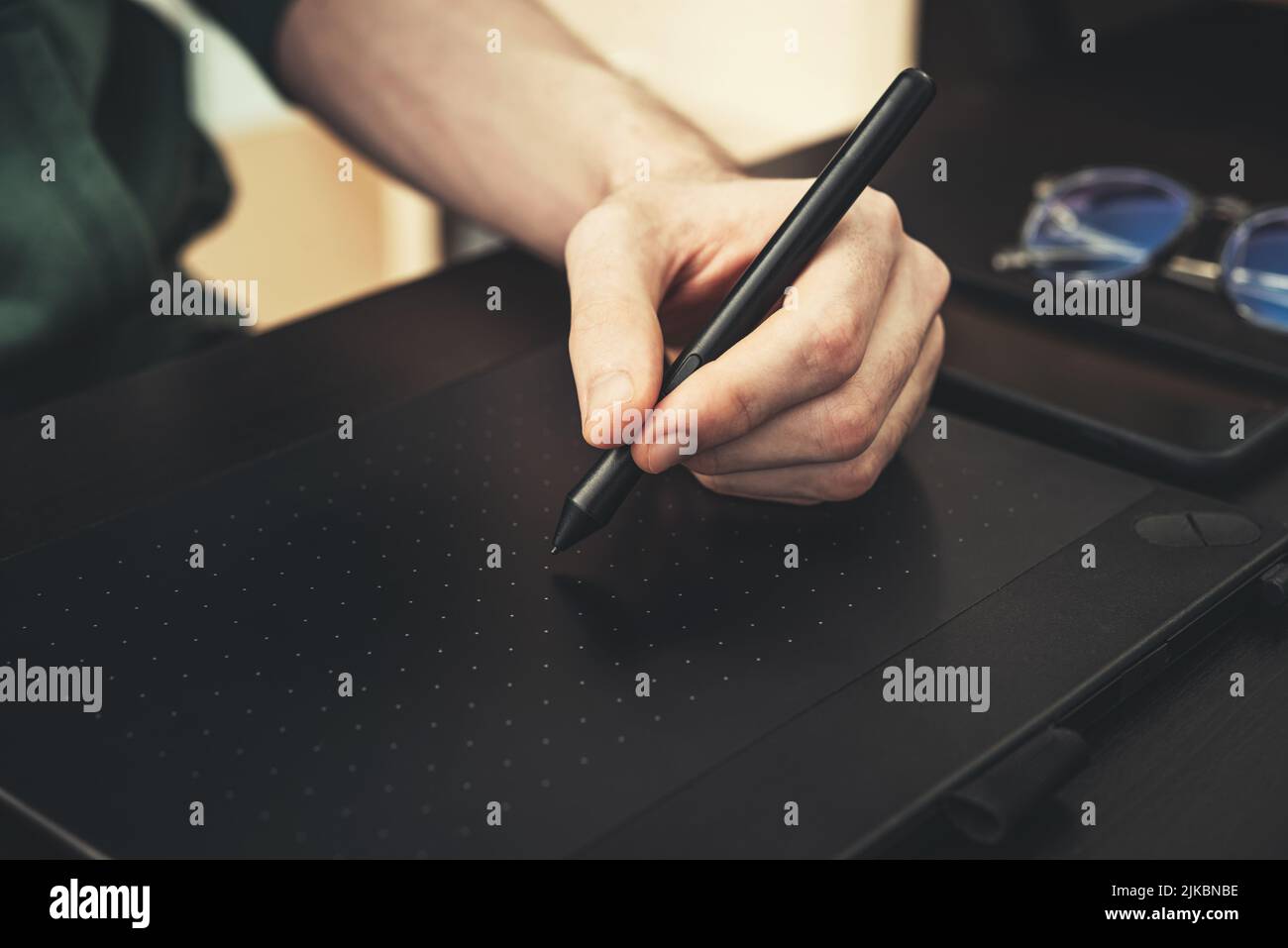 Junger Grafikdesigner, der in Nahaufnahme des Heimbüros ein Grafiktablett auf einem schwarzen Tisch verwendet. Stockfoto