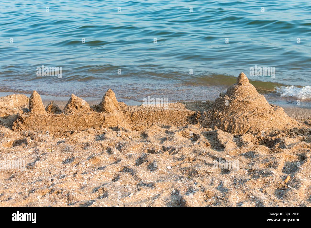Sandburg mit Muscheln an einem Sommerstrand vor dem Hintergrund des Meeres gebaut. Stockfoto