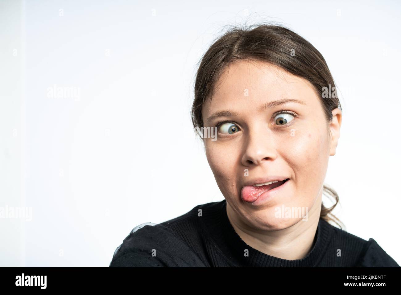 Glückliche junge Frau, die lustige Gesichter macht, auf weißem Hintergrund schwarz trägt, Studioaufnahme Stockfoto