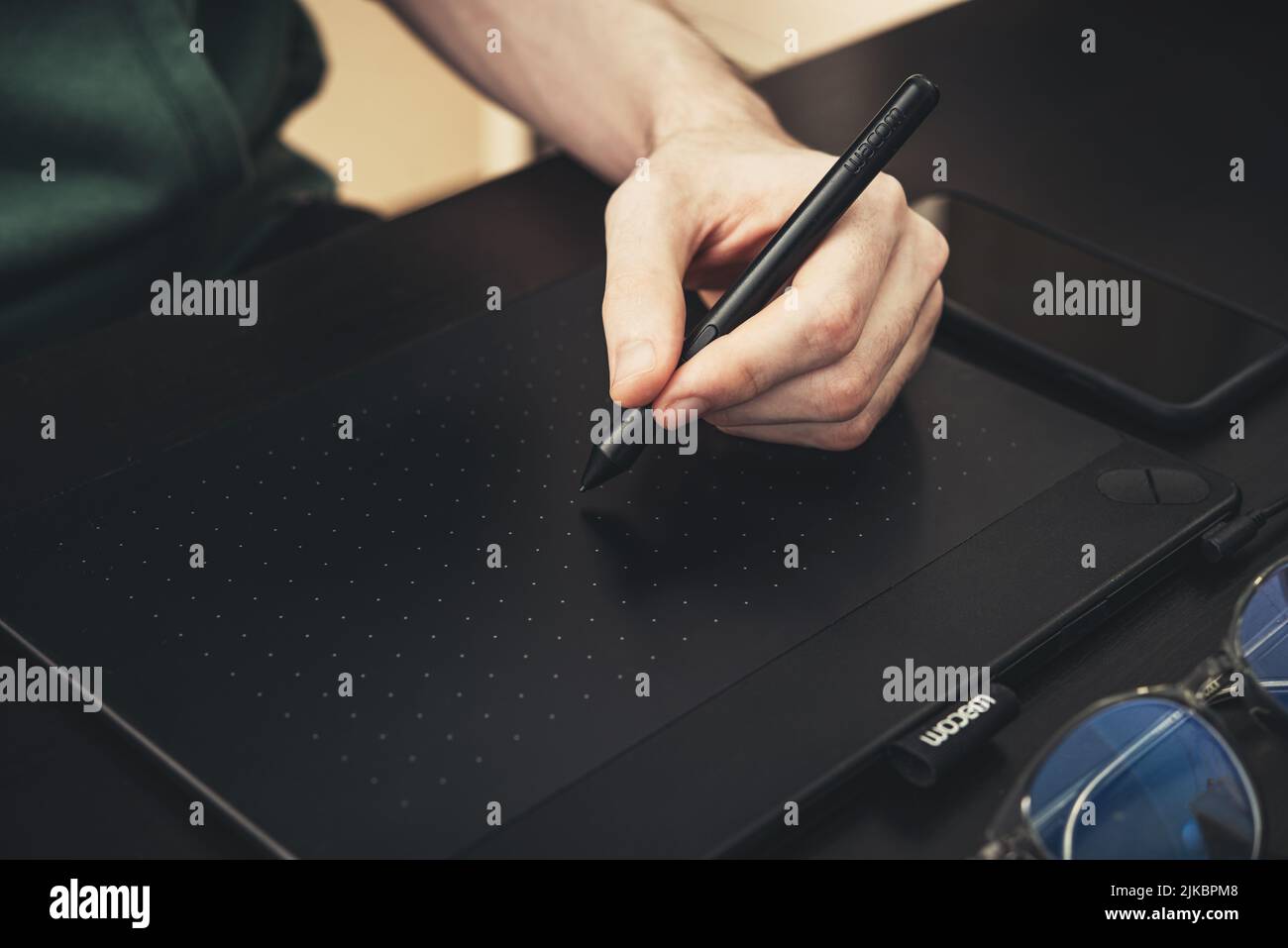 KIEW, UKRAINE - 21. DEZEMBER 2021: Junger Grafikdesigner, der das Wacom-Grafiktablett auf einem schwarzen Tisch in Nahaufnahme des Heimbüros verwendet. Stockfoto