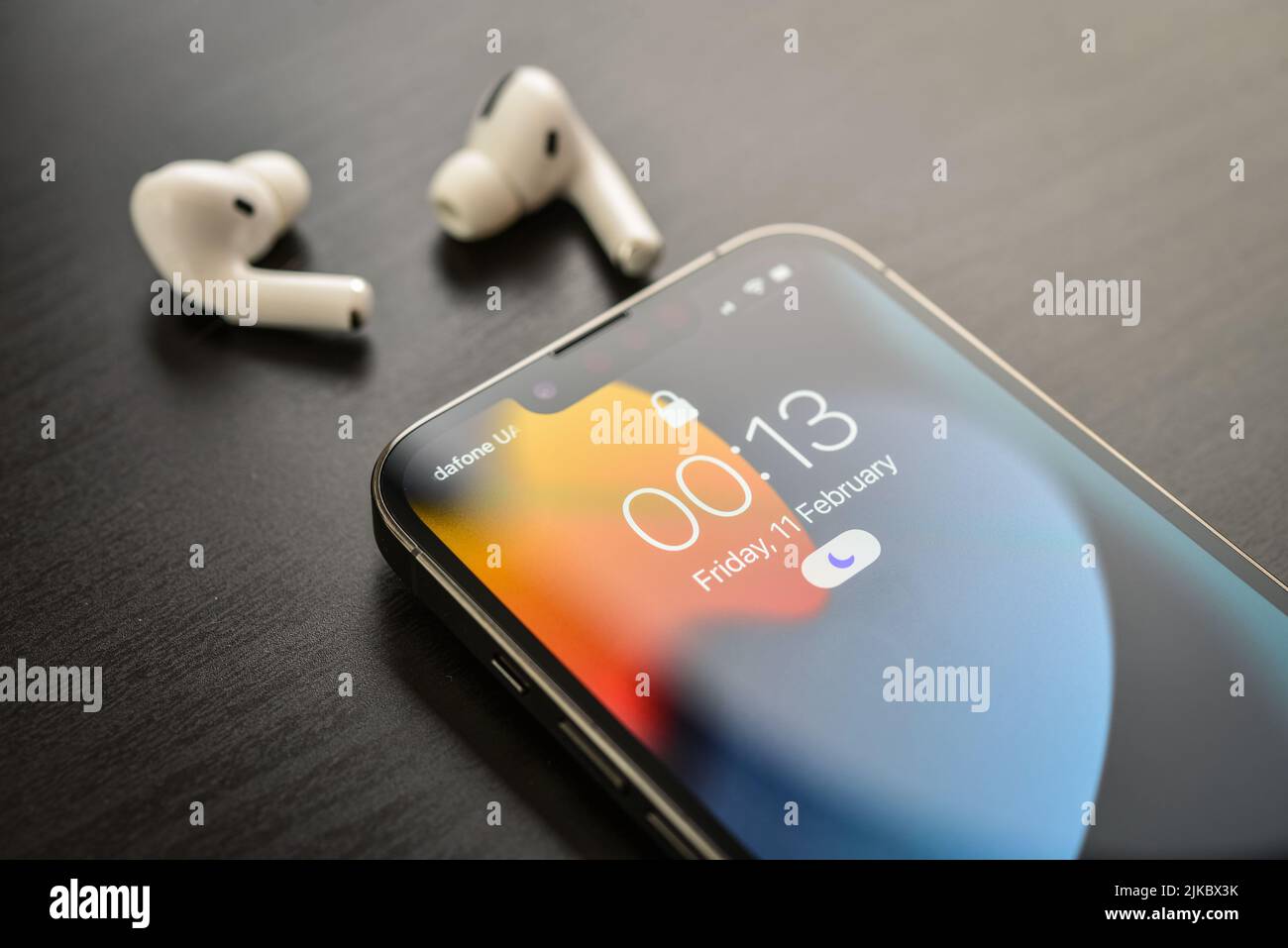 KIEW, UKRAINE - 10. FEBRUAR 2022: Ausgepacktes neues Apple iPhone 13 Pro Space Grey mit AirPods Pro Kopfhörern auf schwarzem Hintergrund. Stockfoto