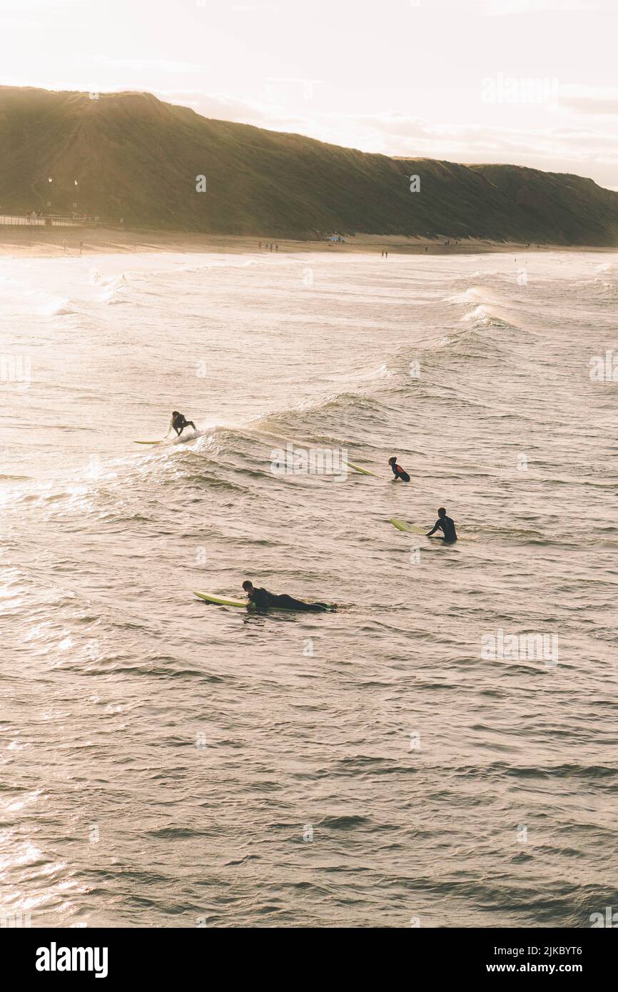 Eine vertikale Aufnahme des Strandes von Saltburn mit Surfern im Meer während der goldenen Stunde Stockfoto