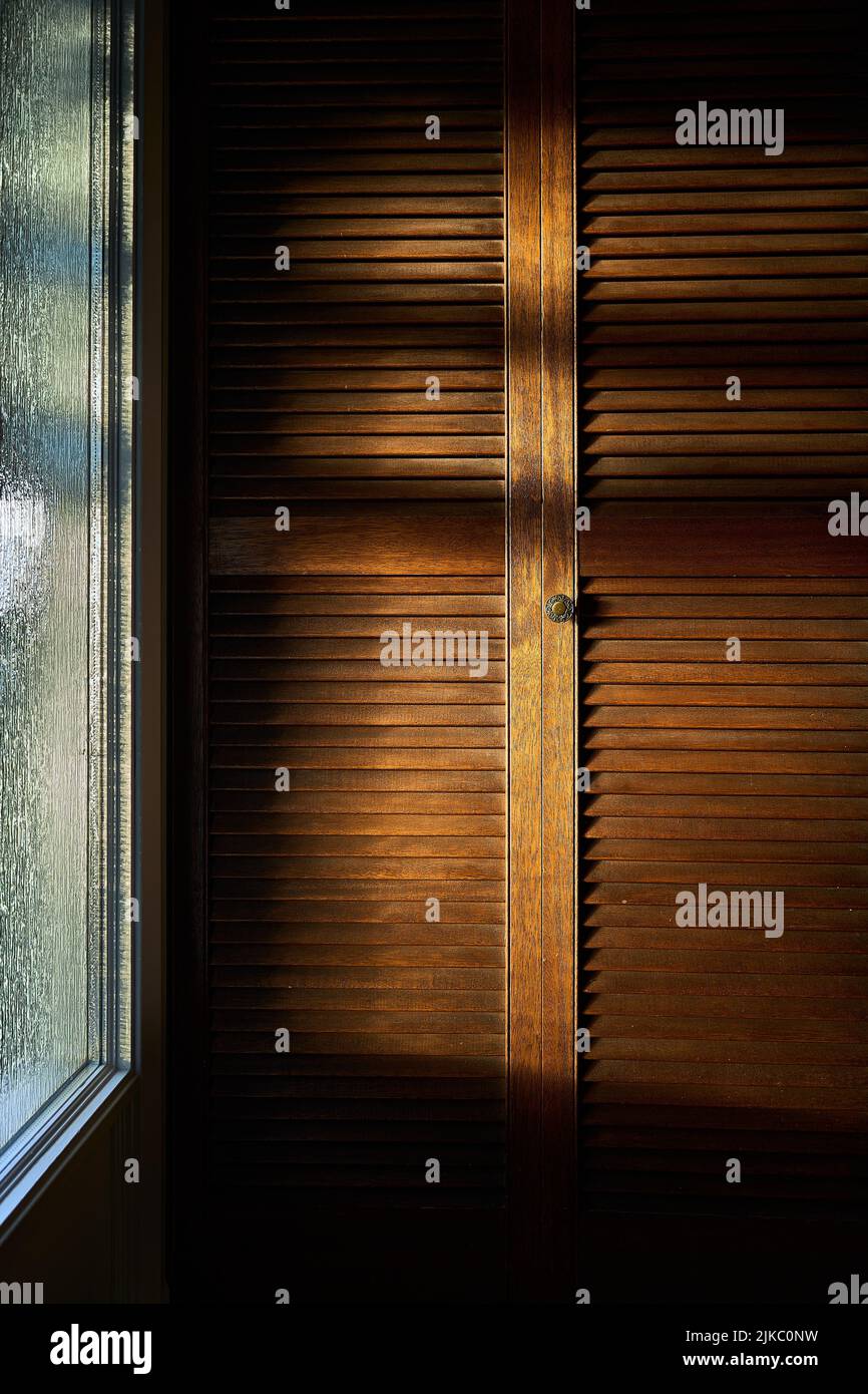 Eine vertikale Aufnahme von Sonnenstrahlen bei Sonnenaufgang durch das Fenster fallen auf die hölzernen Schranktüren Stockfoto