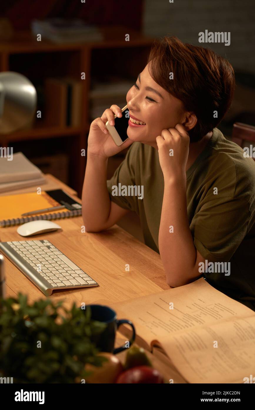 Erwachsene Studentin, die am Schreibtisch sitzt und gerne am Telefon spricht Stockfoto