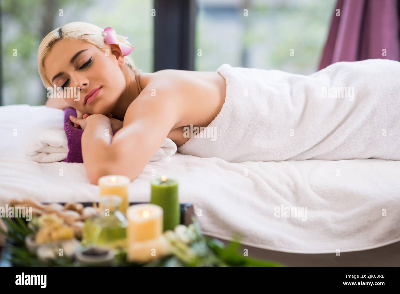 Profilansicht einer attraktiven jungen Frau, die auf einem Massageliegen mit geschlossenen Augen liegt, während sie ein Wochenende im Wellnesscenter verbringt Stockfoto