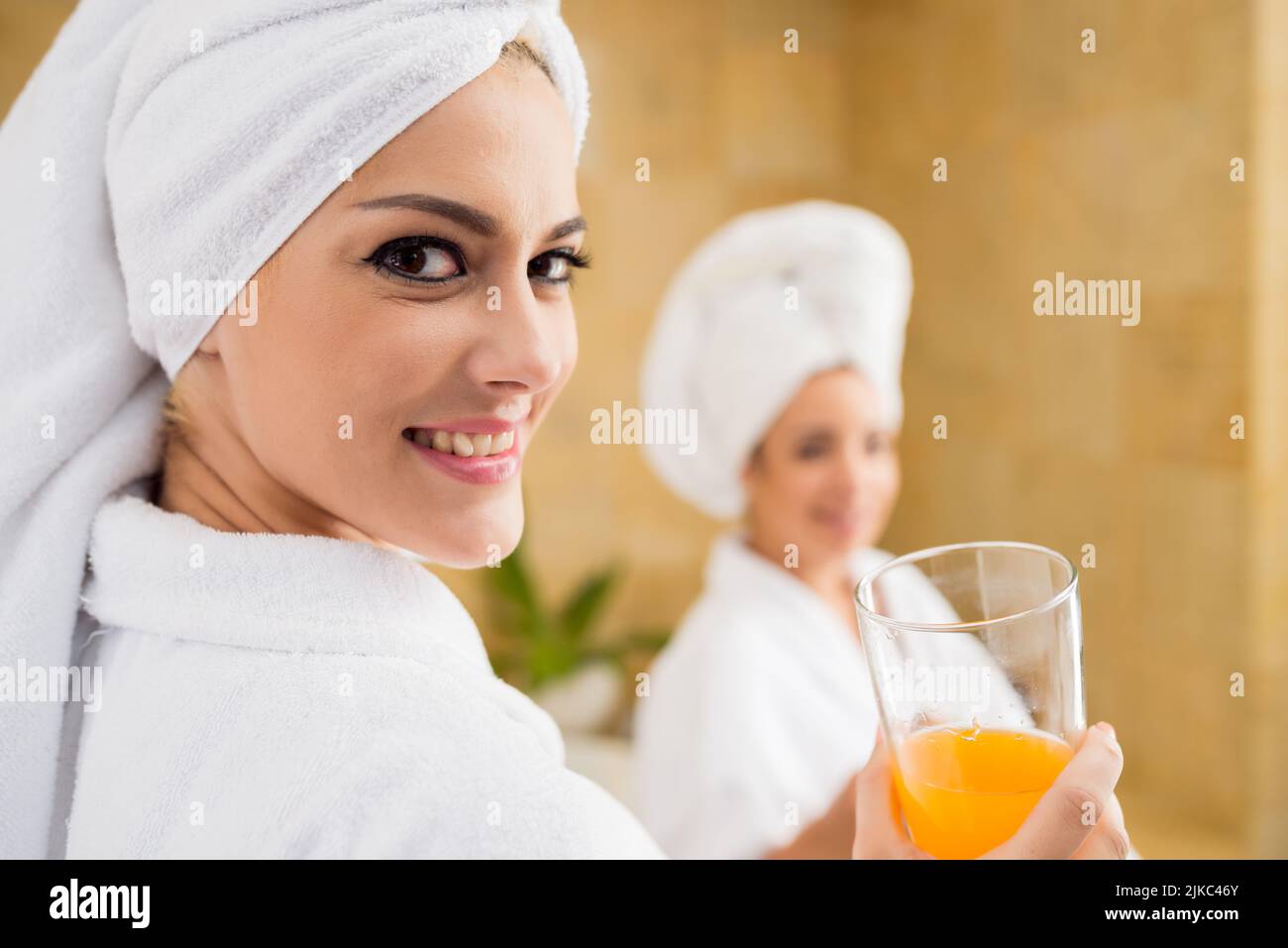Headshot einer attraktiven jungen Frau, die Handtuch und Bademantel trägt und mit toothy Lächeln auf die Kamera blickt, während sie das Wochenende im Wellness-Center genießt, weibliche Silhouette hinter ihr Stockfoto