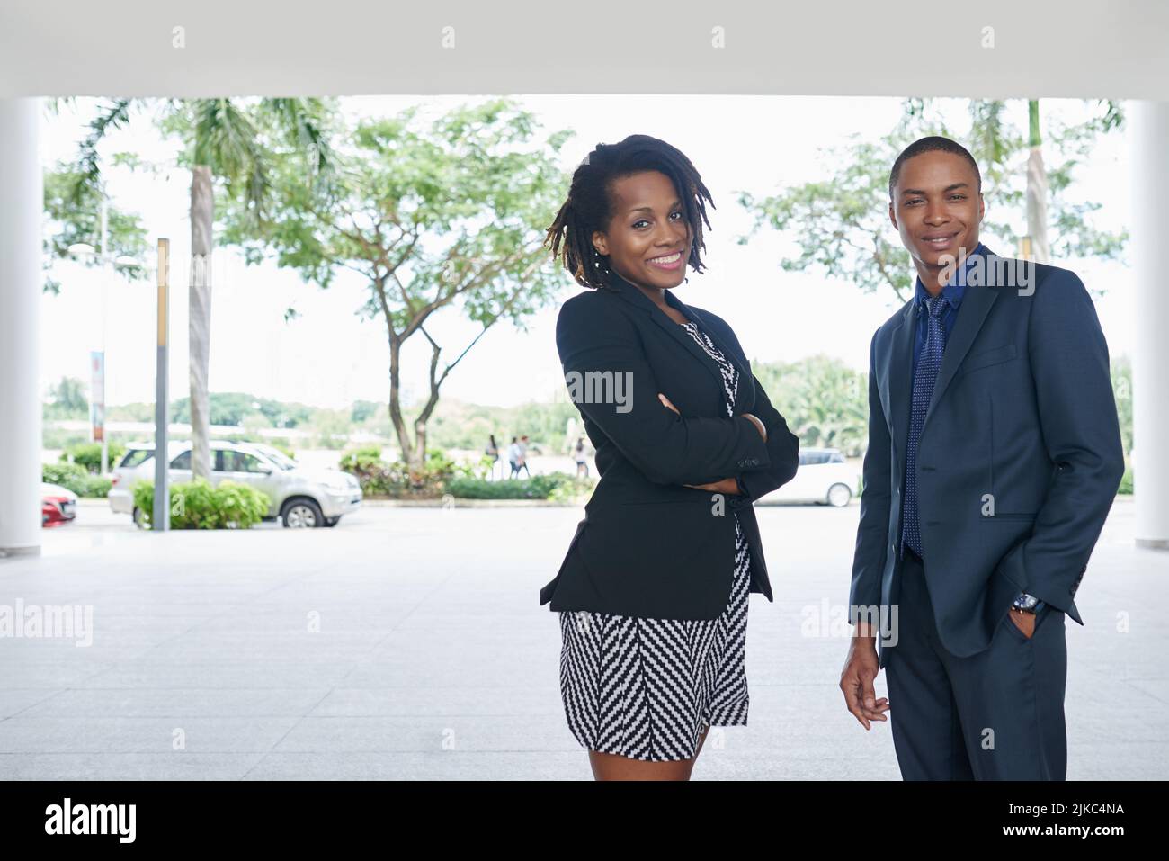 Attraktive junge Angestellte mit weißem Kragen und ihr gutaussehender Mitarbeiter, die mit toothy Lächeln auf die Kamera blicken und dabei die frische Luft im Freien genießen Stockfoto