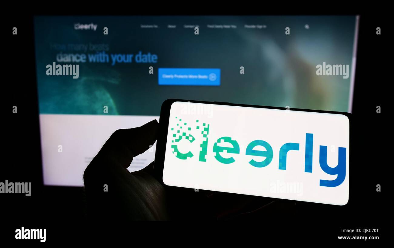 Person, die Mobiltelefon mit dem Logo des US-amerikanischen Gesundheitsunternehmens Cleerly Inc. Auf dem Bildschirm vor der Business-Webseite hält. Konzentrieren Sie sich auf die Telefonanzeige. Stockfoto