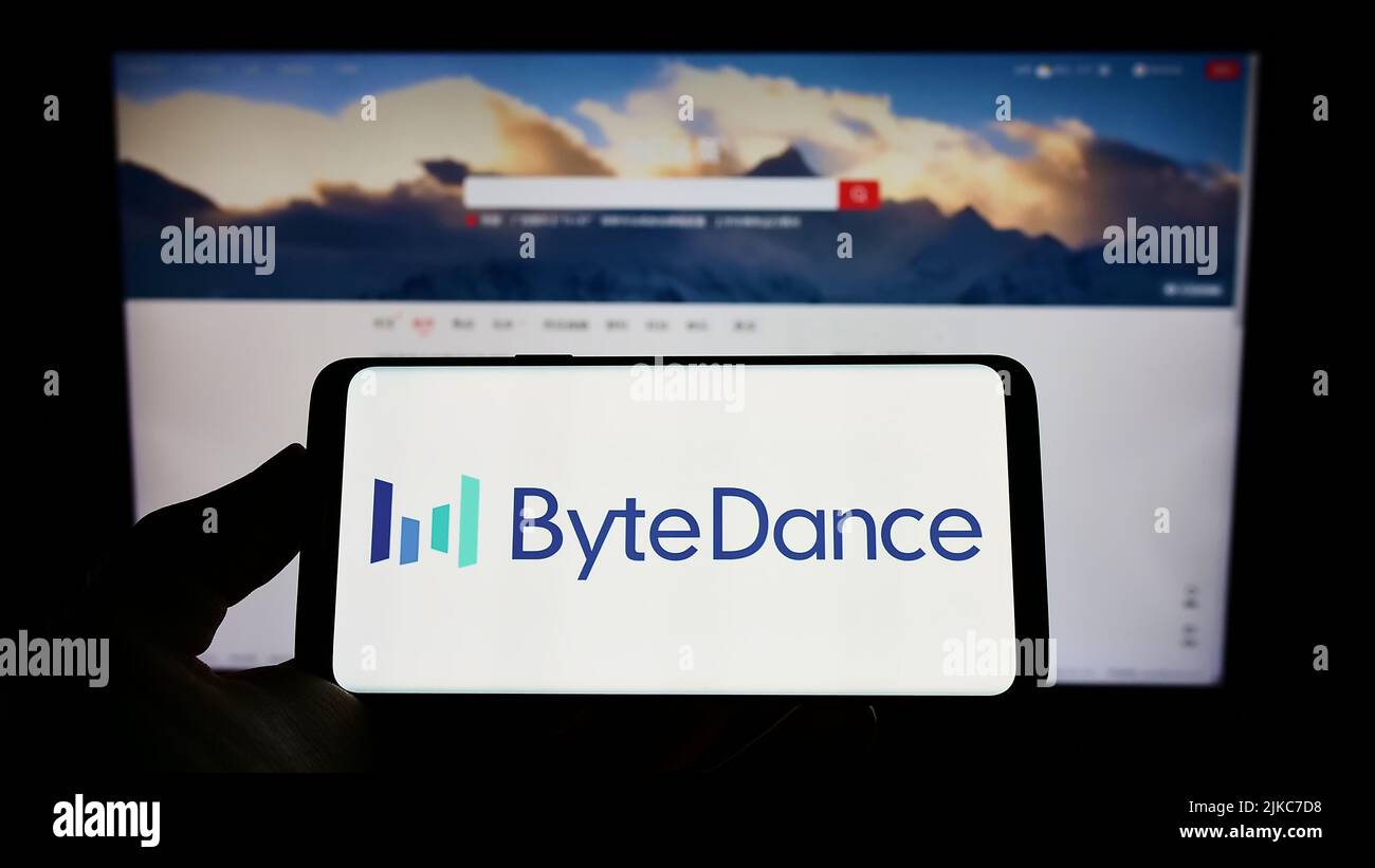 Person, die Mobiltelefon mit dem Logo des chinesischen Technologieunternehmens Bytedance Ltd. Auf dem Bildschirm vor der Business-Webseite hält. Konzentrieren Sie sich auf die Telefonanzeige. Stockfoto