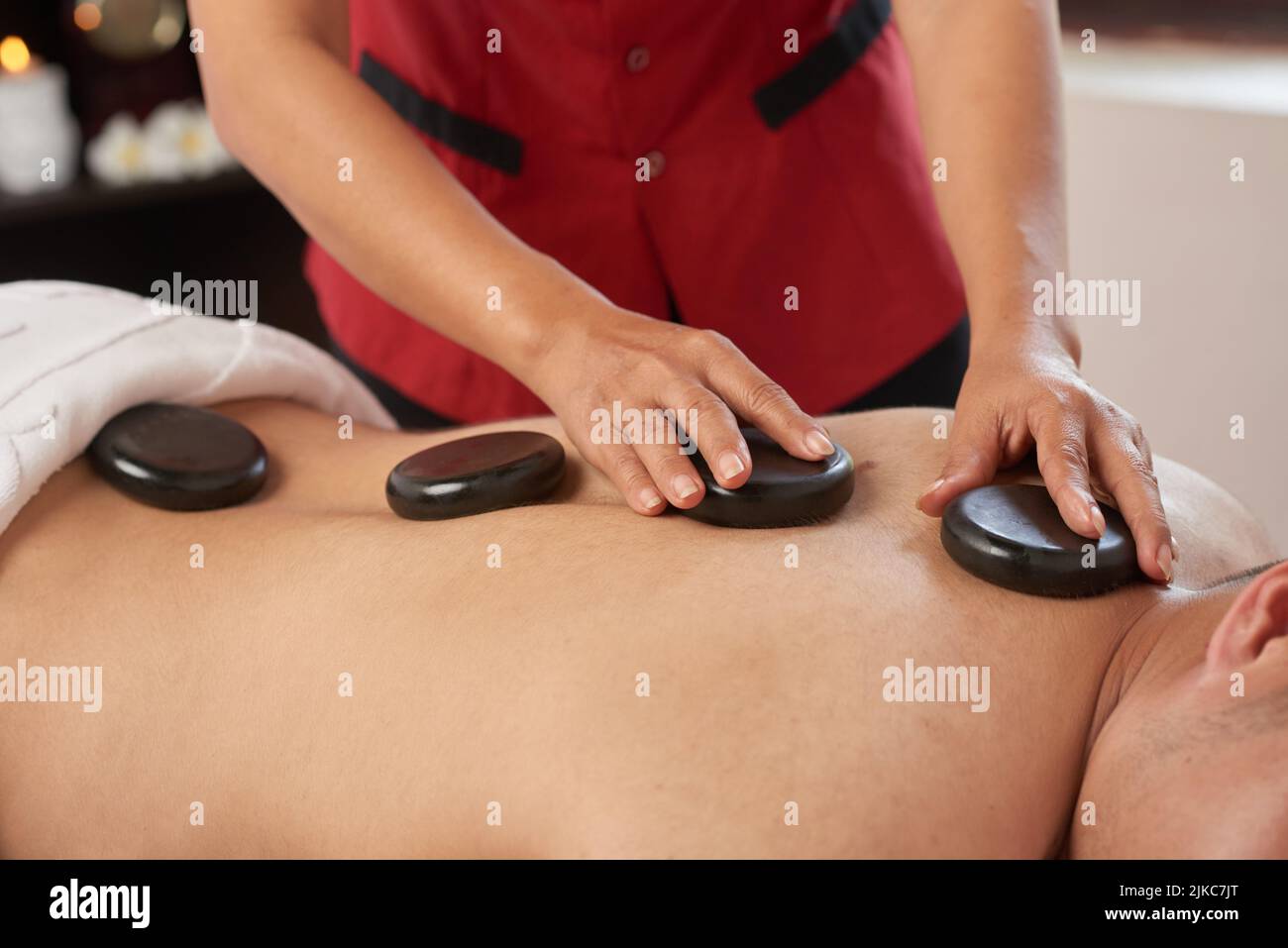 Nahaufnahme eines unverkennbaren Mannes, der während des Wochenendes in einem luxuriösen Spa-Salon eine Hot-Stone-Massage genießt Stockfoto