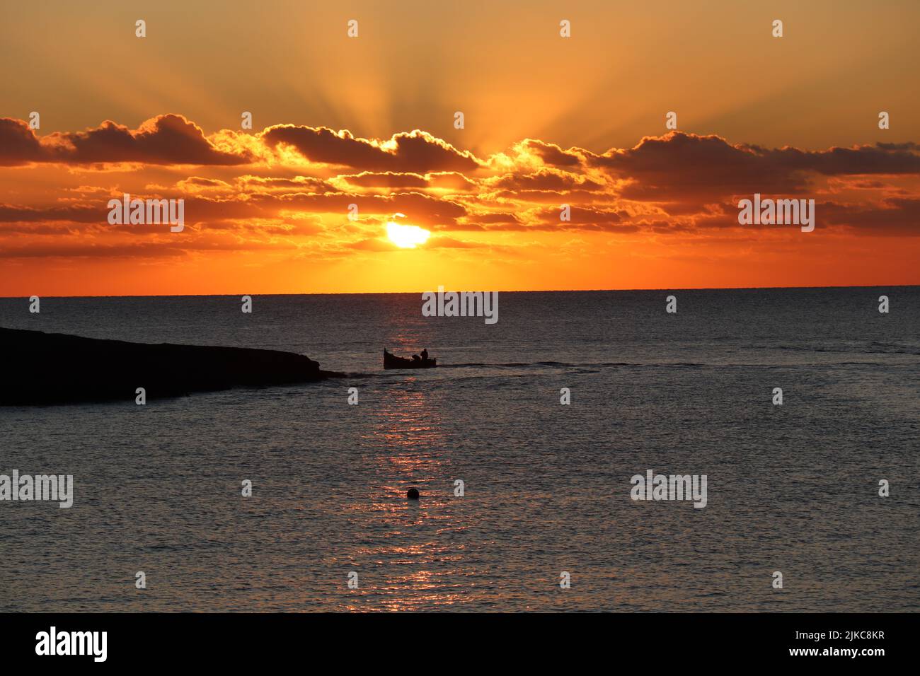 Atemberaubende mediterrane Insel Sonnenuntergang an der Küste mit Blick auf das Meer mit einem Boot Stockfoto