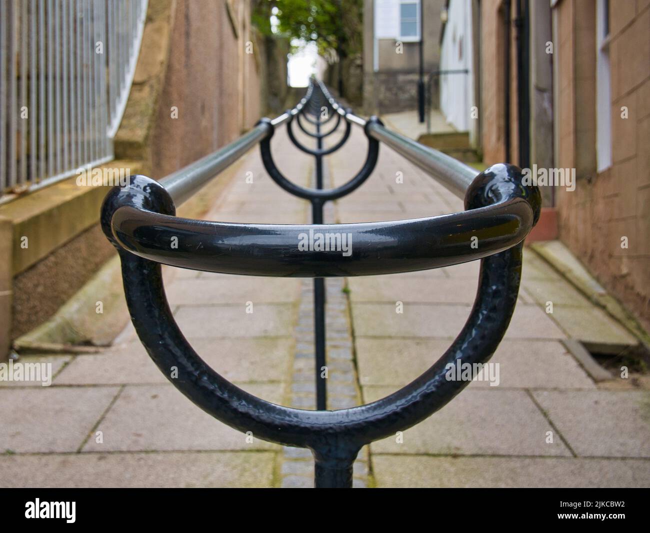 Ein doppelter Metallhandlauf führt einen steilen Gehweg mit Granitfelsen zwischen Gebäuden in Lerwick, Shetland, Großbritannien, hinauf. Stockfoto