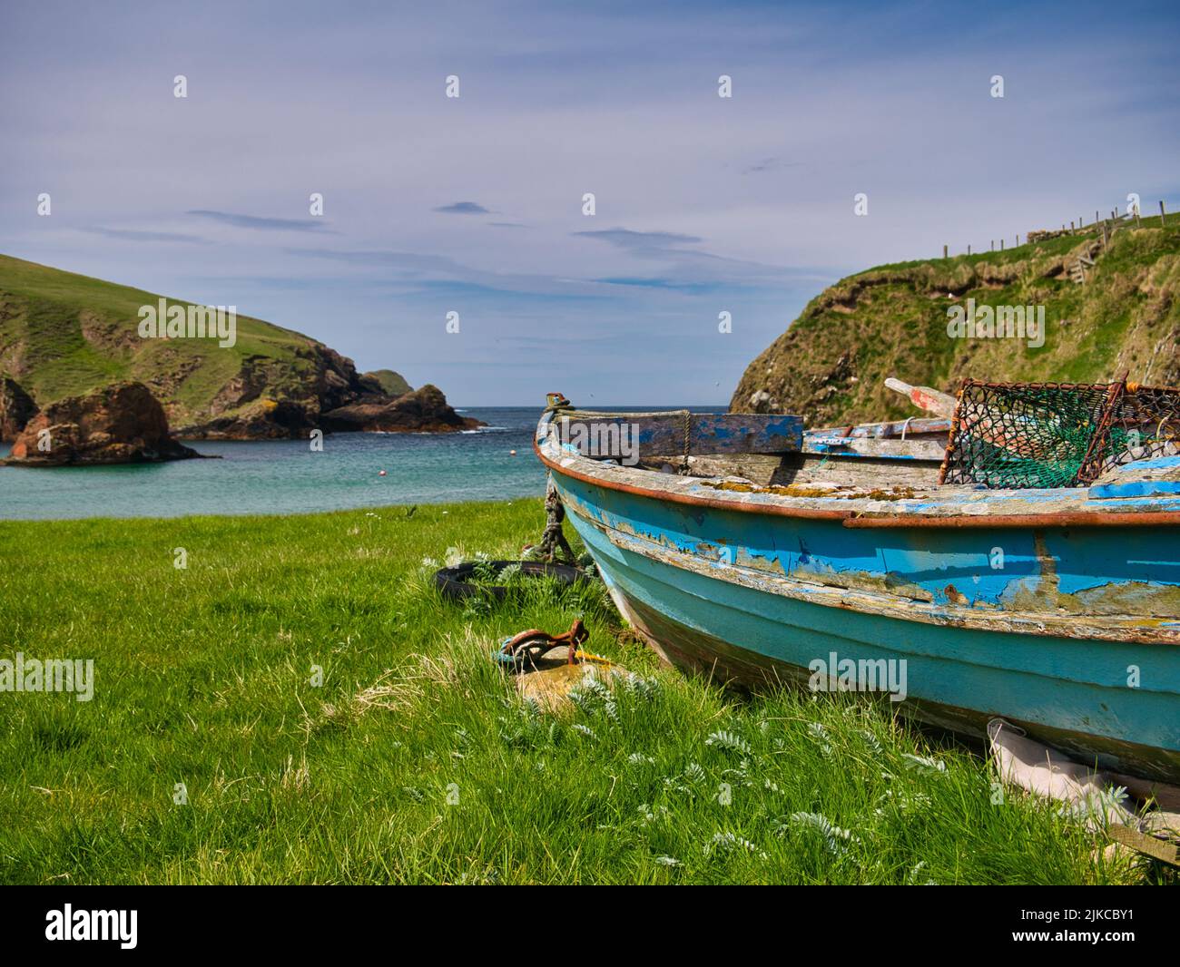Ein altes, verlassenes, blaues Fischerboot aus Holz in der Nähe eines Strandes im Süden von Shetland, Großbritannien. Verwitterte Ruder und ein rostfreier Felsspieler sind an Bord zu sehen. Stockfoto