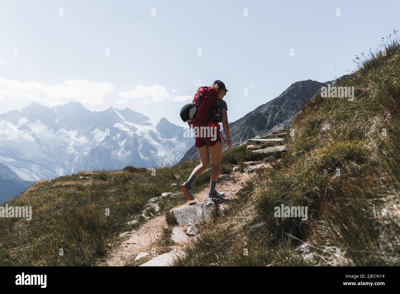 Wandererin mit Rucksack, die vor den Bergen bergauf geht Stockfoto