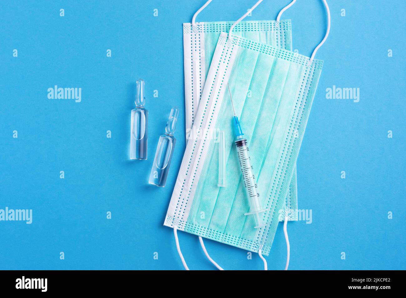 Sterile Medizin Hintergrund mit Injektionsampullen, scharfe Nadel und schützende Gesichtsmasken auf sauberen blauen Schreibtisch. Impfkonzept. Stockfoto