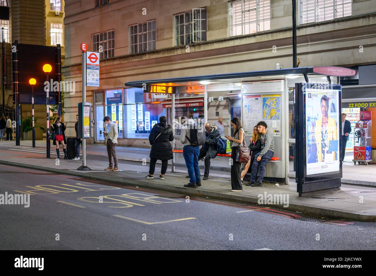 LONDON - 17. Mai 2022: Nachts warten Menschen an einer Londoner Bushaltestelle Stockfoto