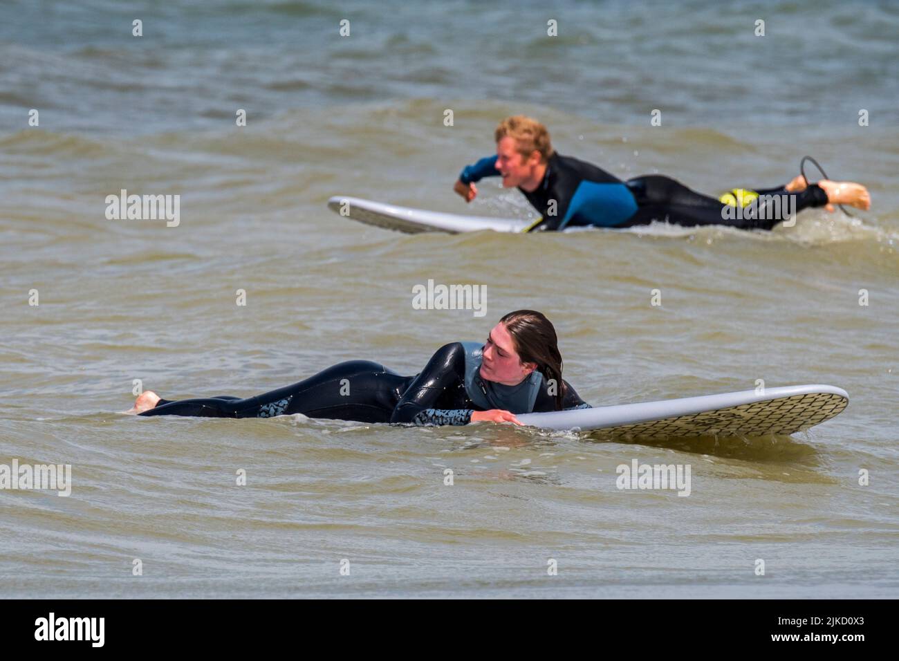 Weibliche Surferin im Neoprenanzug liegt und wartet auf ihrem Surfbrett auf eine große Welle / Breaker, um entlang der Nordseeküste zu surfen Stockfoto