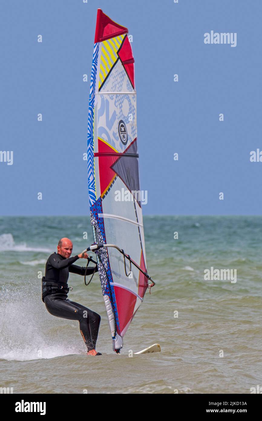 Windsurfer in schwarzem Neoprenanzug üben klassisches Windsurfen entlang der Nordseeküste Stockfoto