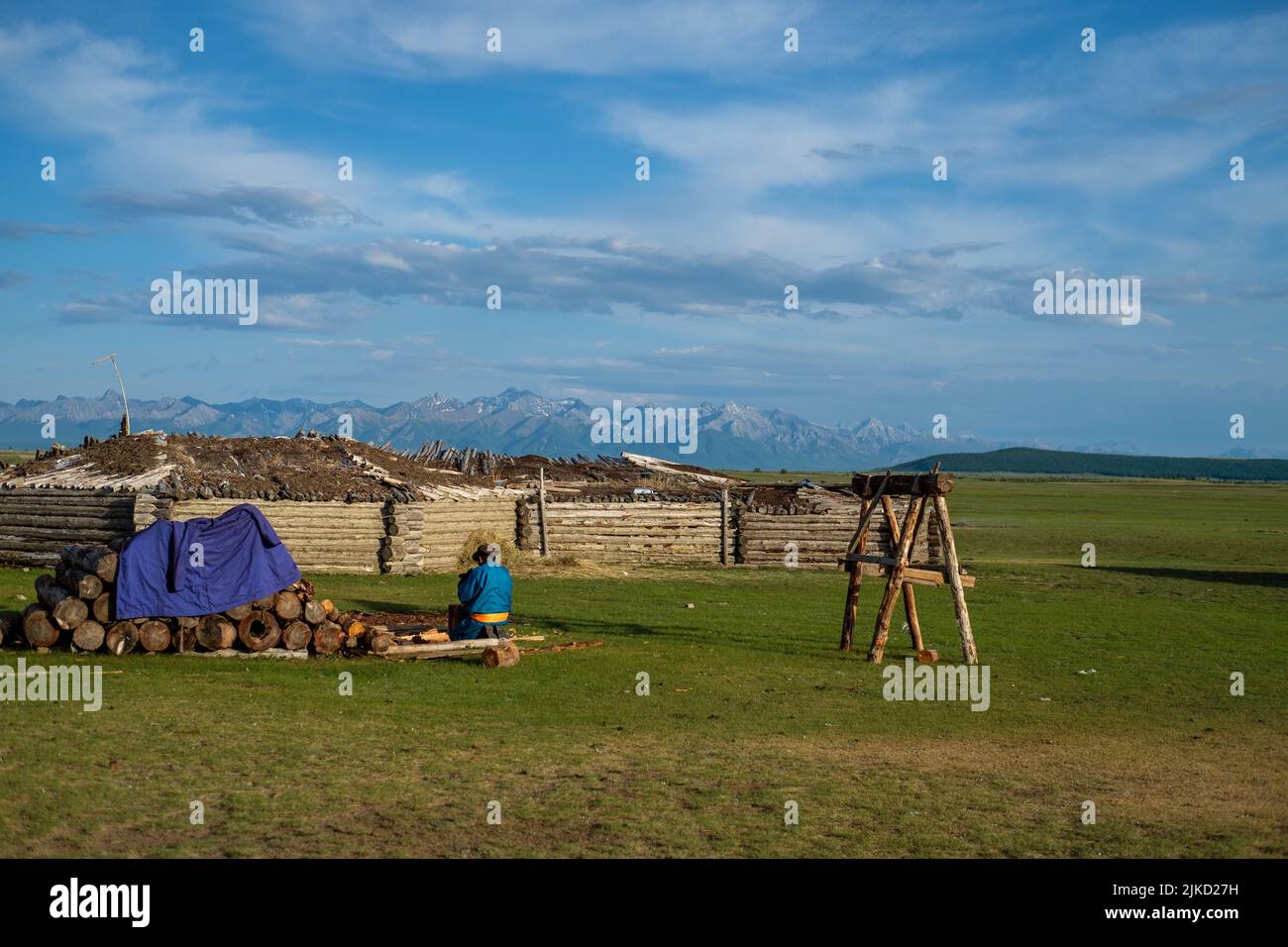 Eine Rückansicht einer Person aus dem Tsaatan-Hüterstamm, die in der ländlichen Mongolei in der Nähe eines Holzstapels sitzt Stockfoto