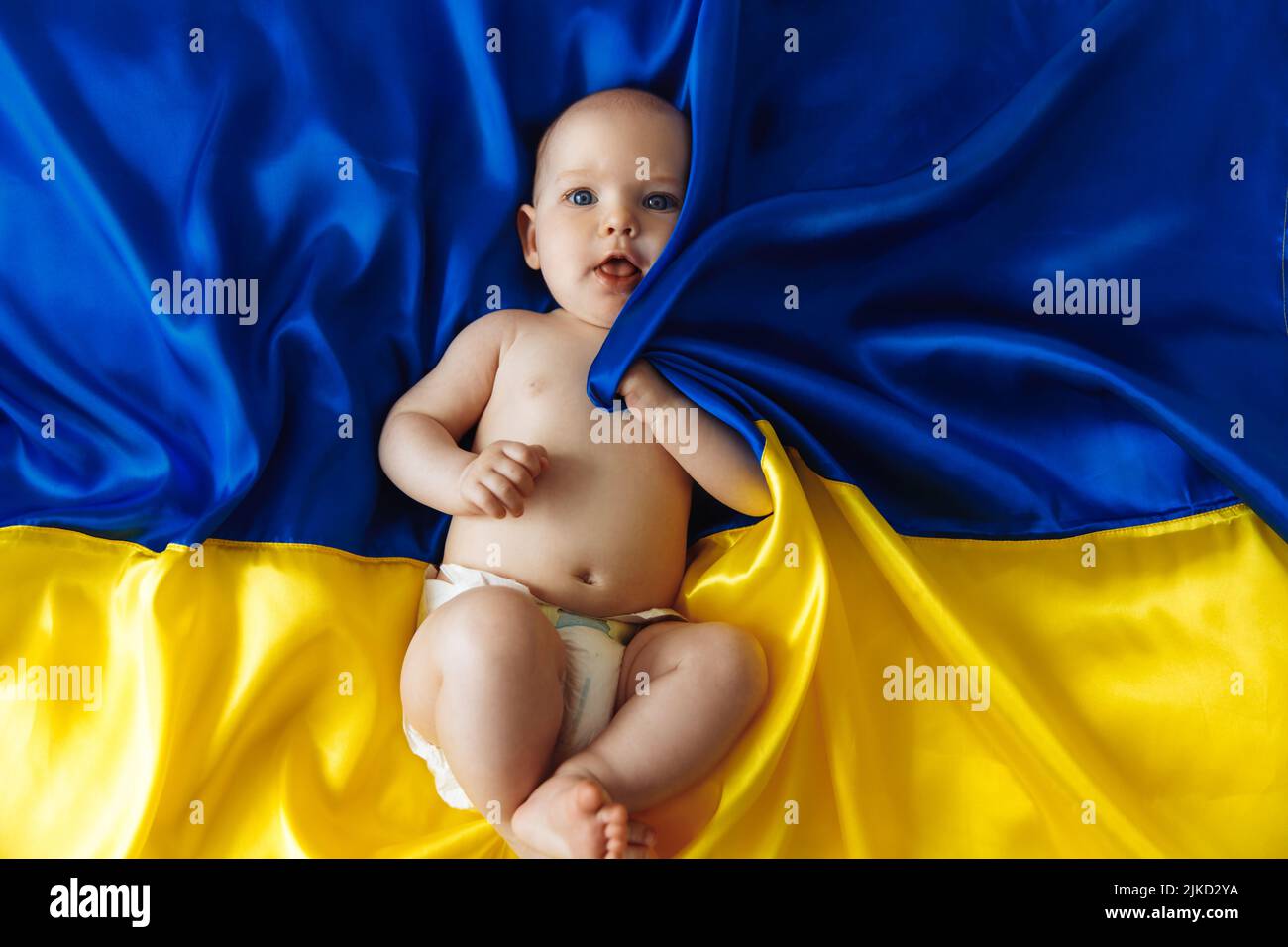 Betet für die Ukraine. Kleines wehrloses Baby liegt auf der blau-gelben ukrainischen Flagge. Protest gegen den Krieg, Krise, Frieden, Ende der Aggression, Kind wieder Stockfoto