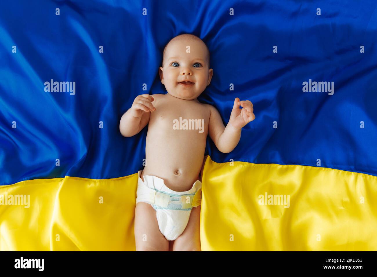 Betet für die Ukraine Ein lächelndes kleines Mädchen liegt auf der blauen und gelben ukrainischen Flagge. Das Kind gibt Hoffnung für das Beste. Protest gegen Krieg, Frieden, Ende Stockfoto