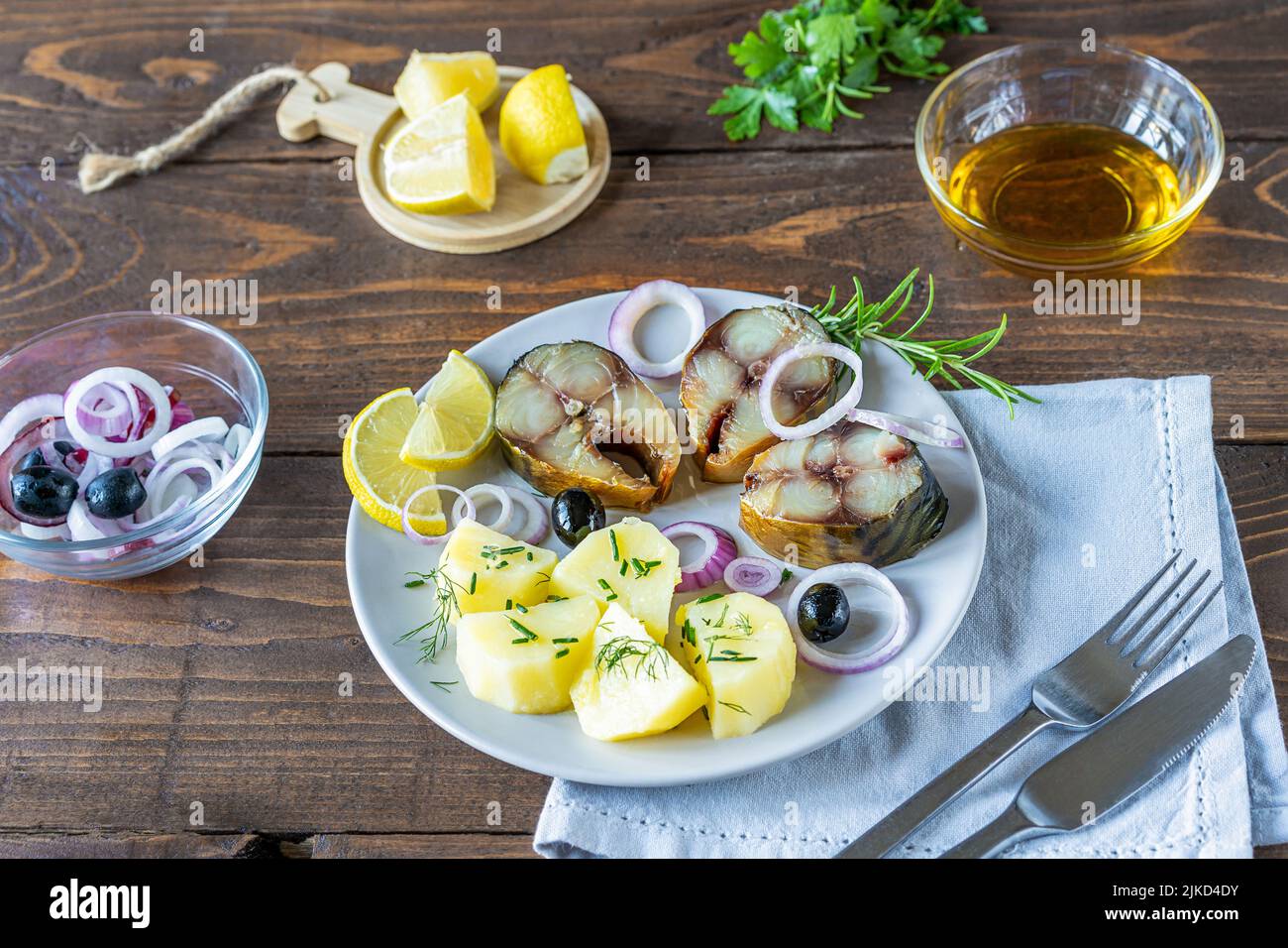 Geräucherte Makrele mit gekochten Kartoffeln, Zwiebelringen, Zitrone, Oliven, Öl auf den Teller schneiden, grüne auf Holzhintergrund Stockfoto