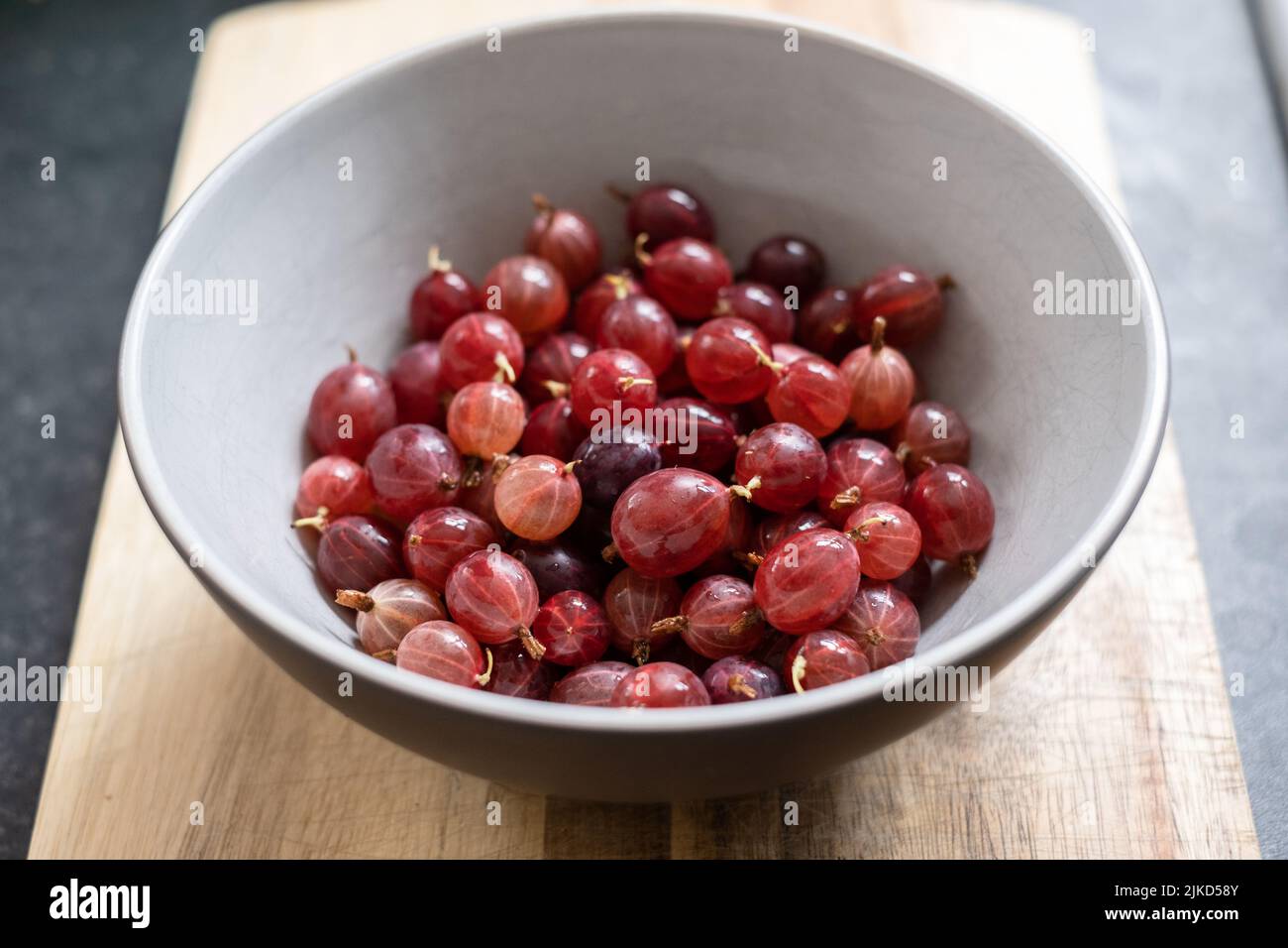 Eine Schüssel mit frisch gepflückten und gewaschenen hausgemachten Hinnonmaki Red Stachelbeeren auf einem Holzbrett. Stockfoto