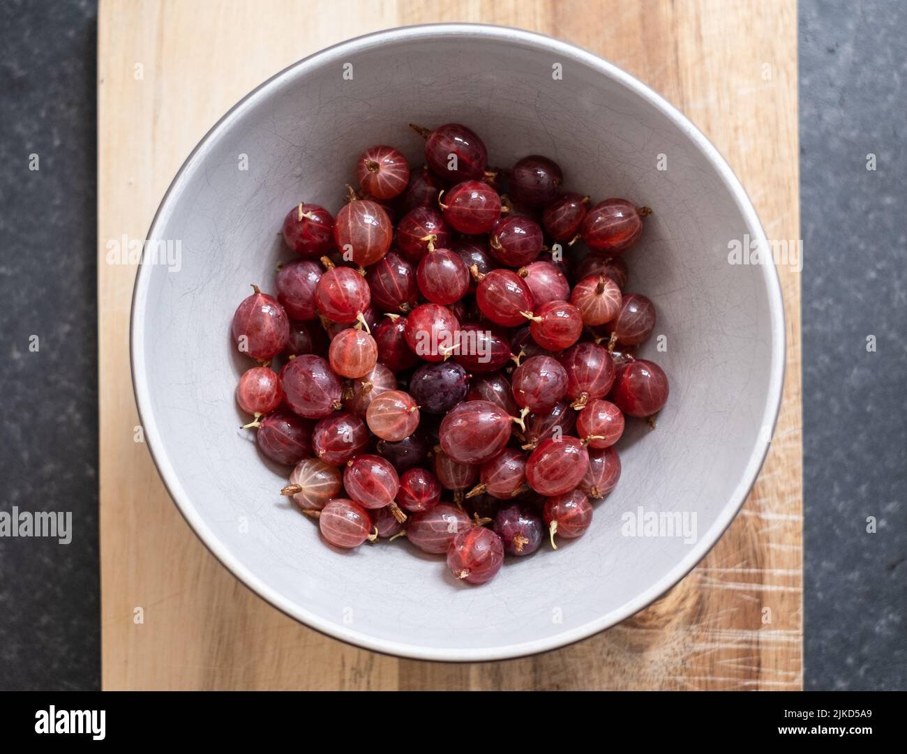 Eine Schüssel mit frisch gepflückten und gewaschenen hausgemachten Hinnonmaki Red Stachelbeeren auf einem Holzbrett. Stockfoto