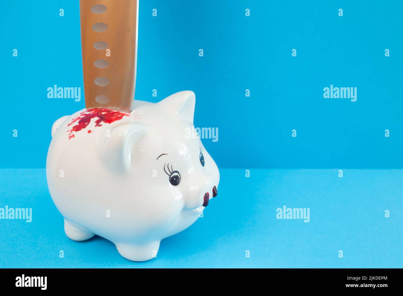 Schweinebank aus Porzellan mit einem Messer im Rücken. Metapher der Finanzkrise, isoliert auf blauem Hintergrund. Stockfoto