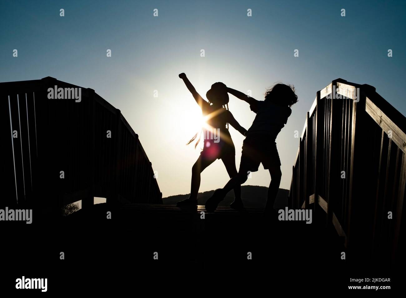 Junge und Mädchen Silhouetten tanzen auf einer Brücke gegen die Sonnenuntergangssonne Stockfoto