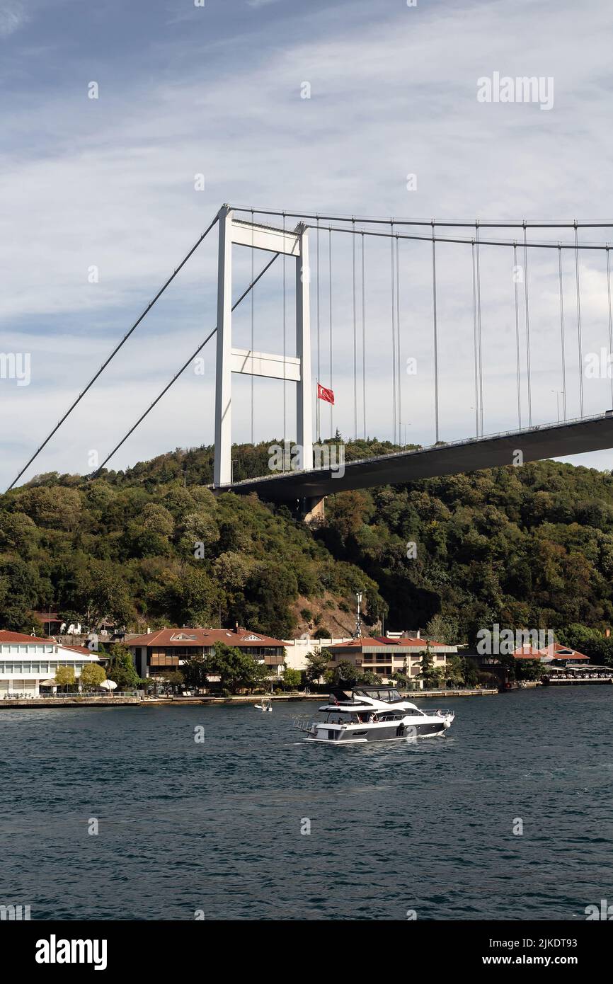 Blick auf die Yacht, die am Bosporus durch das Kanlica-Viertel auf der asiatischen Seite Istanbuls vorbeifährt. Die FSM-Brücke ist im Hintergrund. Es ist ein sonniger Sommertag. Beaut Stockfoto