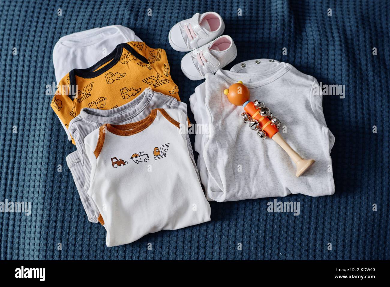 Kollektion von neuer Casualwear für zukünftige Babys, winzigen weißen Lederschuhen und Spielzeug auf blauem Textilhintergrund oder Bett mit Samtbezug Stockfoto