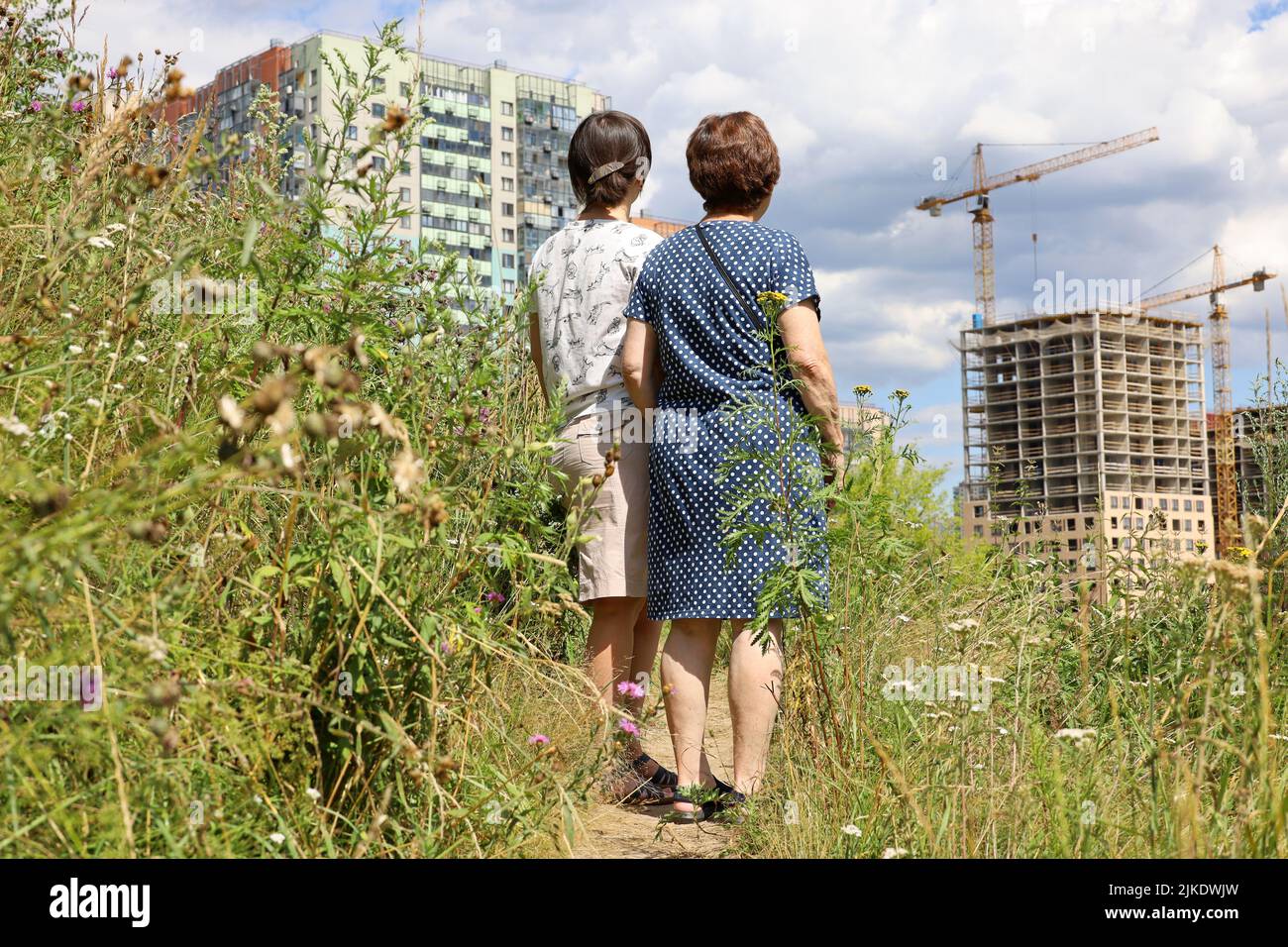 Zwei Frauen stehen auf grünem Rasen und schauen sich die neuen Häuser von Wohnbezirks- und Baukranen an. Käufer, die eine Wohnung wählen Stockfoto