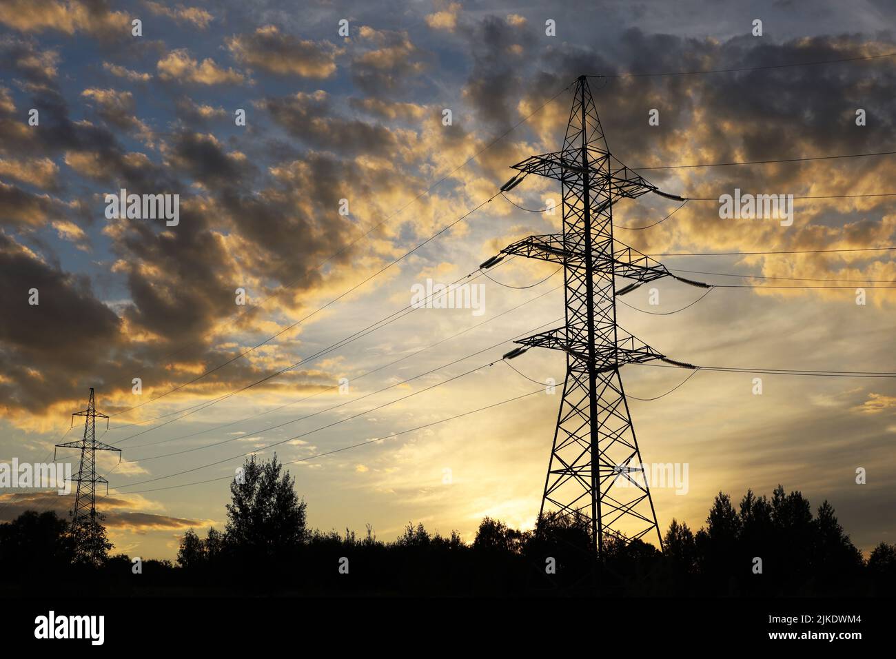 Silhouetten von Hochspannungstürmen mit elektrischen Drähten auf dem Hintergrund des Sonnenuntergangs Himmel und dunklen Wolken. Stromübertragungsleitungen im Abendwald Stockfoto