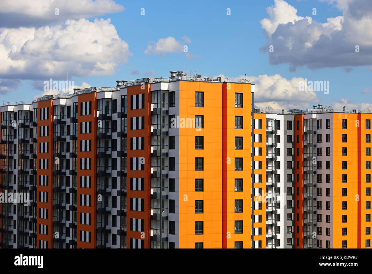 Neue Wohngebäude mit orangefarbenem Futter und blauem Himmel mit weißen Wolken. Hausentwicklung, Hochhausbau Stockfoto
