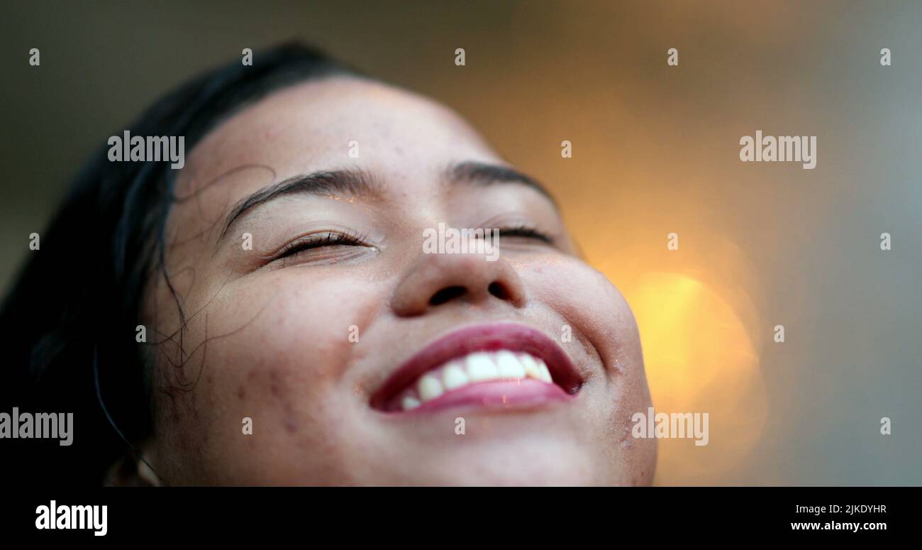 Junge Frau, die im Regen steht, lächelt mit geschlossenen Augen und fühlt, dass Tröpfchen auf das Gesicht fallen und die kleinen Dinge im Leben genießen Stockfoto