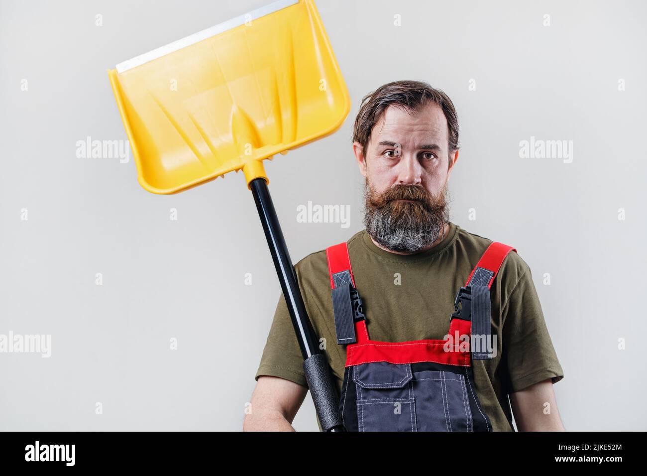Bärtiger Mann in Overalls mit einer Schneeschaufel. Stockfoto
