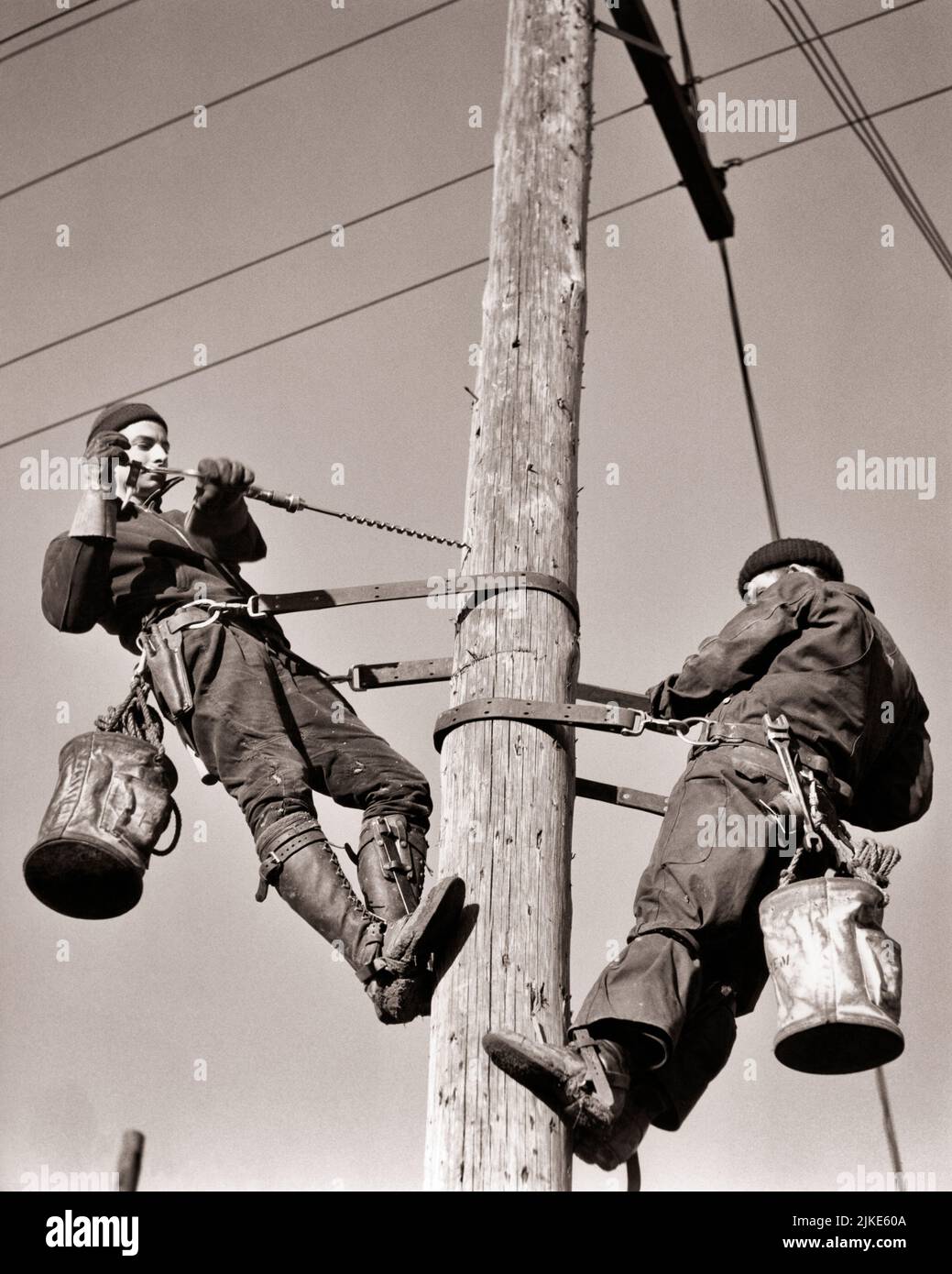 1930S ZWEI MÄNNER ELEKTRISCHE LINIENZÜGE INSTALLATION VON STROMLEITUNGEN AUF EINEM HÖLZERNEN STROMMAST - I3343 HAR001 HARS ARBEIT BESSERE BESCHÄFTIGUNGSLINIEN BERUFE INFRASTRUKTUR MITARBEITER EINRICHTUNGEN KERN LINIENZÜGE MID-ADULT MID-ADULT MAN SYSTEME JUNGER ERWACHSENER MANN SCHWARZ-WEISS KAUKASISCHE ETHNIZITÄT WIRTSCHAFT HAR001 INSTALLATION LABORING ALTMODISCH Stockfoto