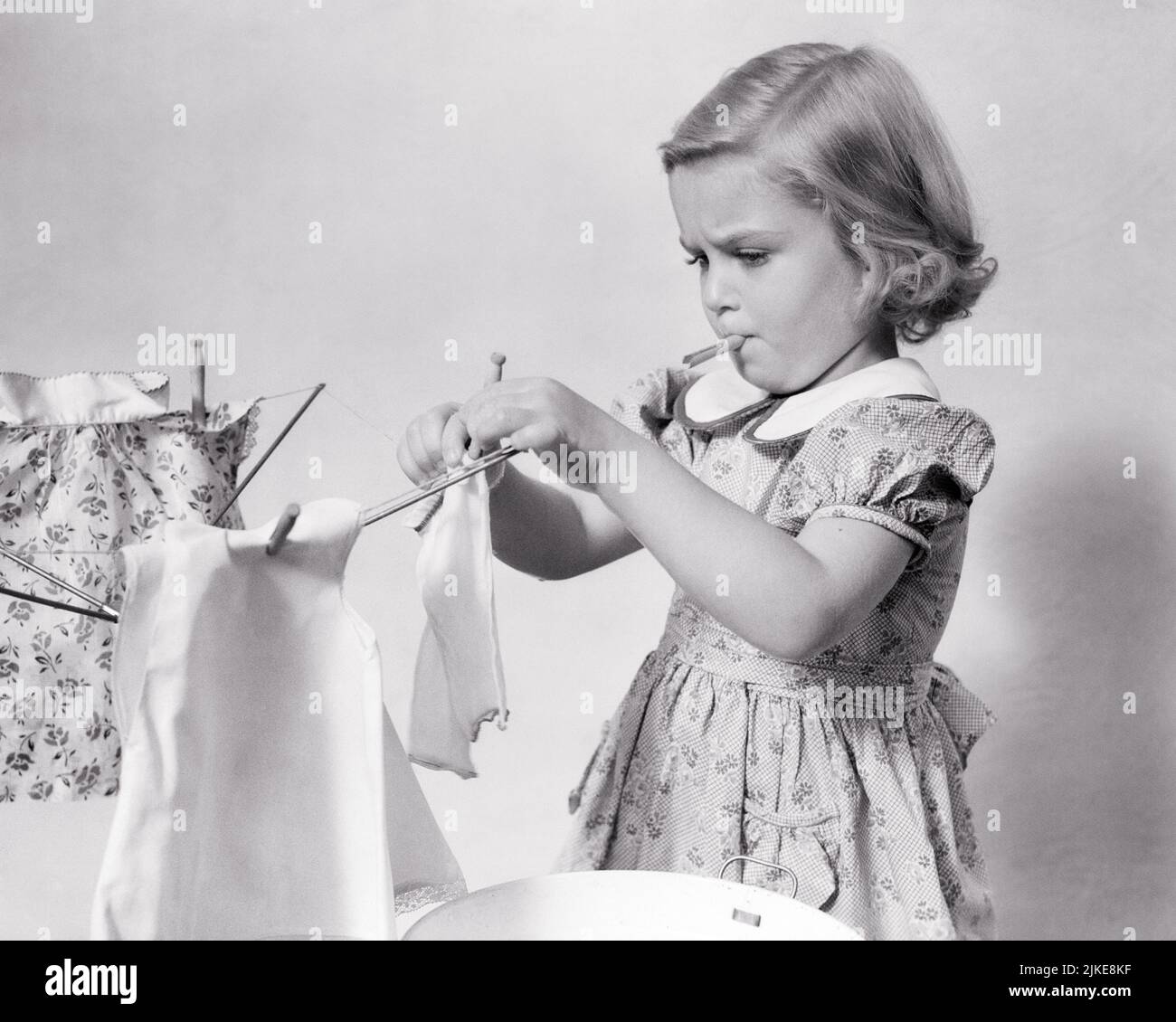 1930S KLEINES MÄDCHEN HÄNGEND IHRE SPIELZEUGPUPPE’S GEWASCHEN KLEIDUNG AUF DER LINIE MIT KLEINEN WÄSCHEKLAMMERN TROCKNEN - J923 HAR001 HARS LIFESTYLE ZUFRIEDENHEIT FRAUEN JOBS LÄNDLICHES HEIM LEBEN KOPIEREN RAUM HALBE LÄNGE INSPIRATION PRAXIS PFLEGE SCHWARZWEISS MINIATUR ZIELE HAUSFRAU GESCHICK BERUF GRÖSSE FÄHIGKEITEN HAUSFRAUEN CHORE ENTDECKUNG WÄSCHELEINE WISSEN GEWASCHENER STOLZ WASHDAY HAUSFRAUEN BERUFE KONZEPTIONELLE STILVOLLE MONTAG PUPPE S WÄSCHEKLAMMERN WACHSTUM JUGENDLICHE SCHWARZ UND WEISSE KAUKASISCHE ETHNIE HAR001 ALTMODISCH Stockfoto