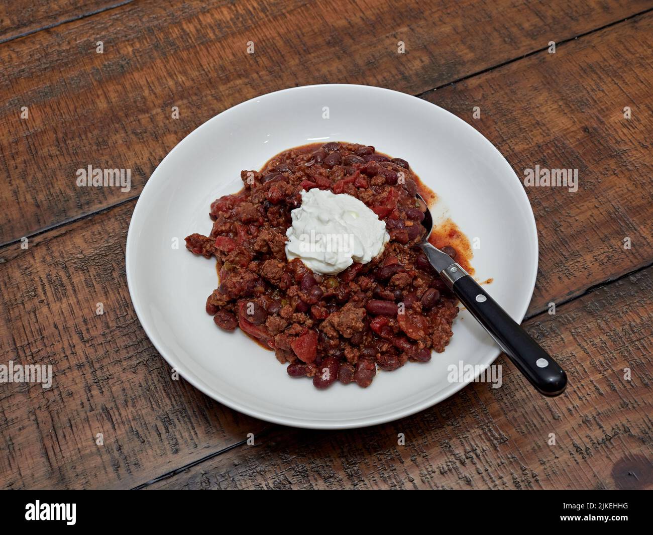 Schüssel mit hausgemachtem Chili mit einem Klecks saurer Creme und einem großen Löffel zum Abendessen oder Mittagessen. Stockfoto