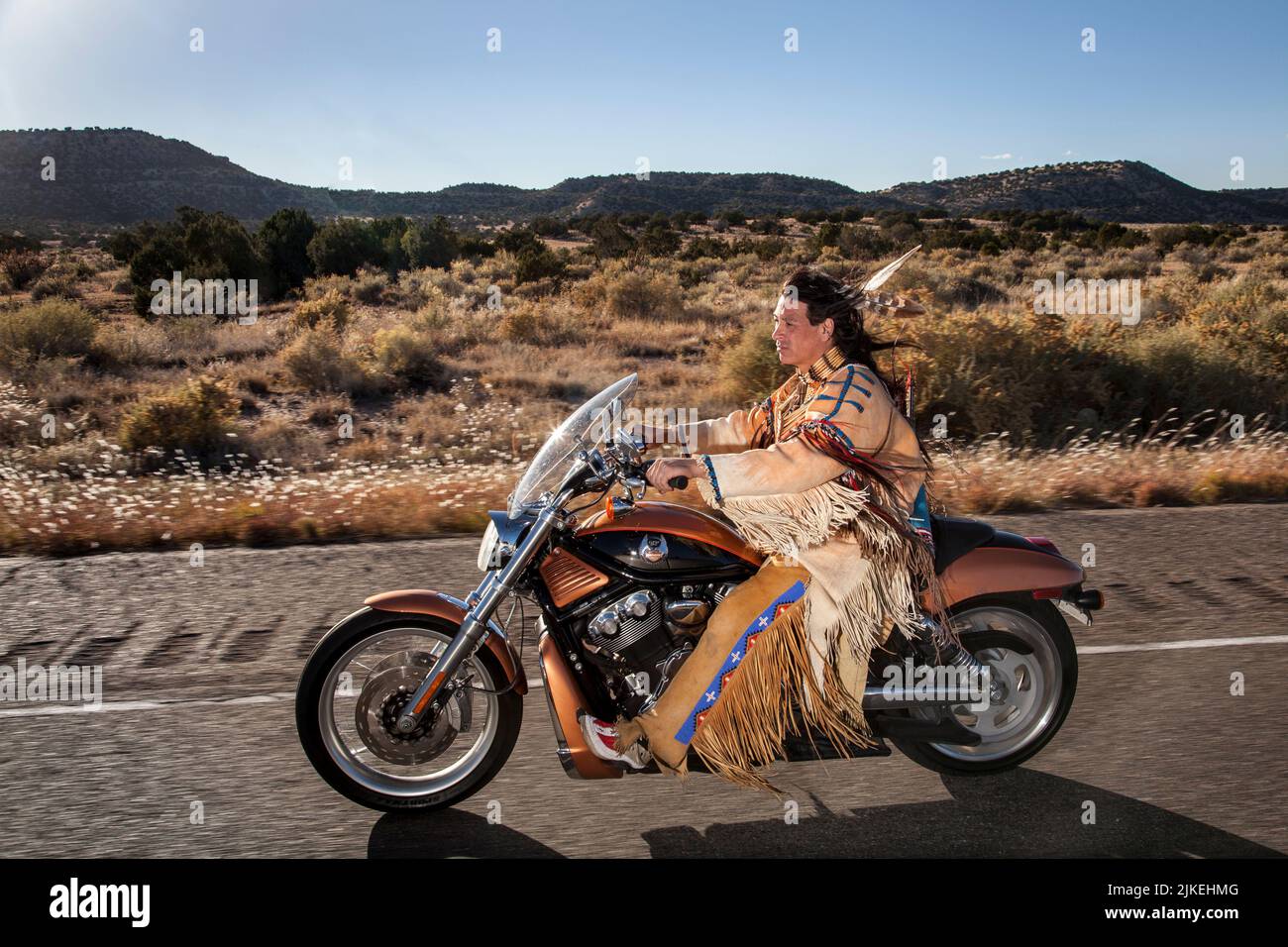 Traditionell gekleideter Indianermann (Arapahoe) fährt Harley Davidson Motorrad auf dem Country Highway Stockfoto