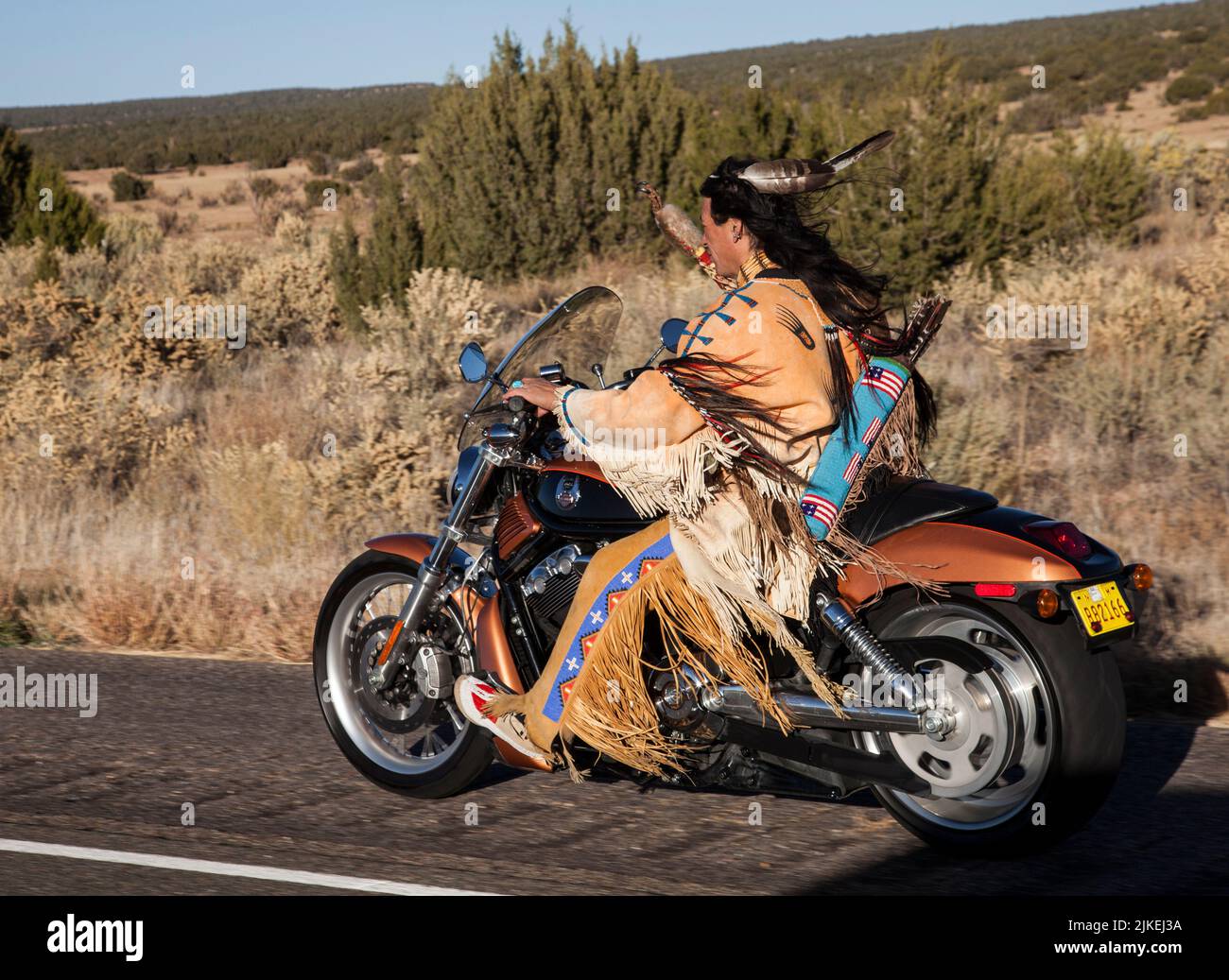 Traditionell gekleideter Indianermann (Arapahoe) fährt Harley Davidson Motorrad auf dem Country Highway Stockfoto