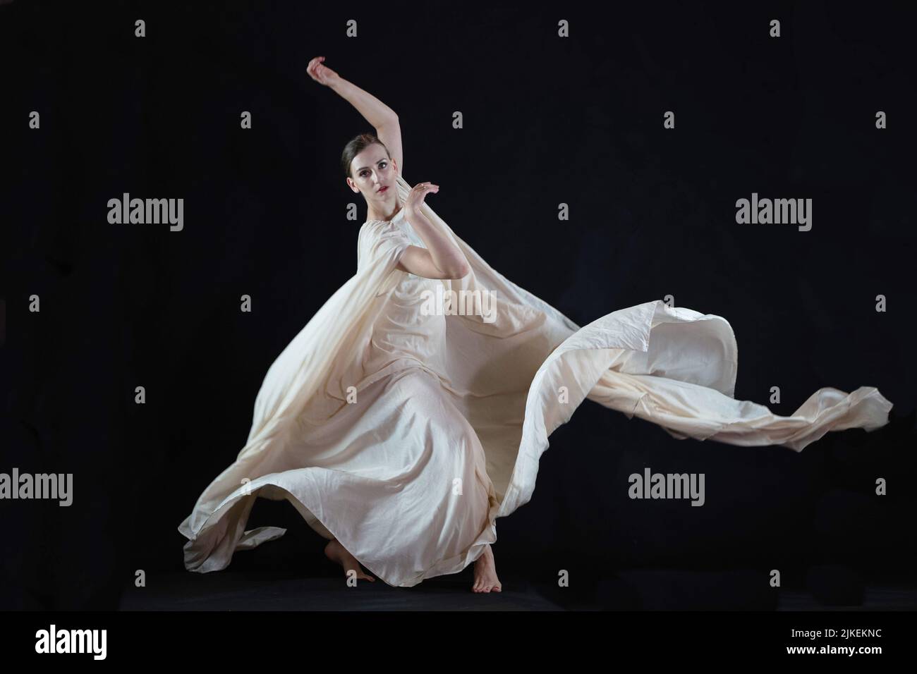 Eine Frau in einer weißen Robe auf schwarzem Hintergrund, eine Tänzerin, dramatischer Tanz Stockfoto