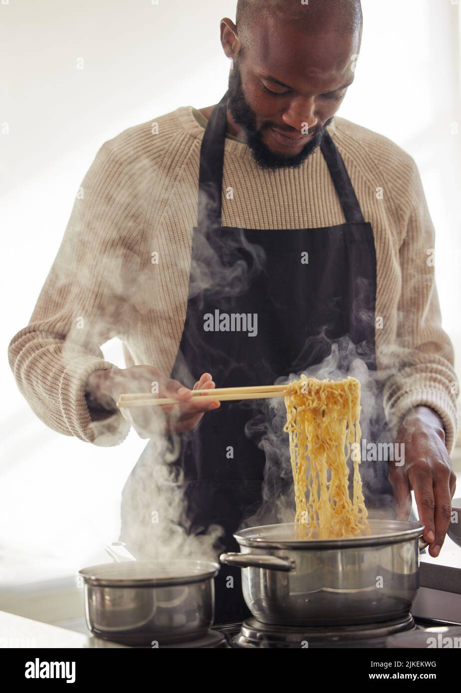 Ramen ist seine Spezialität. Ein hübscher junger Mann kocht auf seinem Herd in der Küche zu Hause. Stockfoto