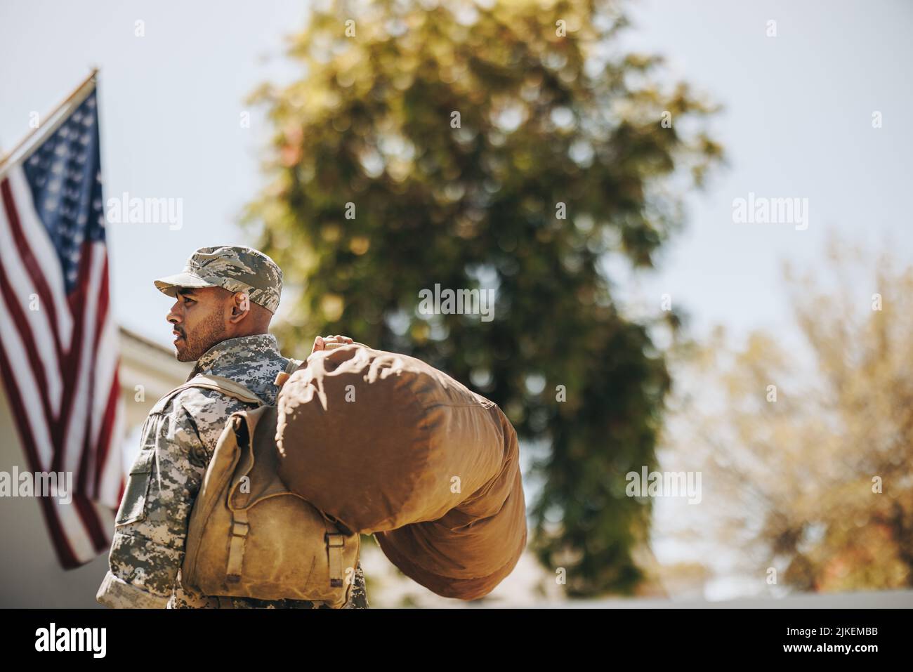 Mutiger junger Soldat, der mit seinem Gepäck auf sein Haus zugeht. Rückansicht eines patriotischen amerikanischen Militäranmannes, der nach seinem Dienst nach Hause zurückkehrt Stockfoto